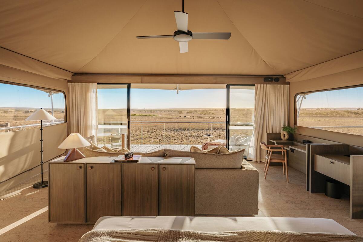 A tented room with a bed, a desk, and a view of the landscape.