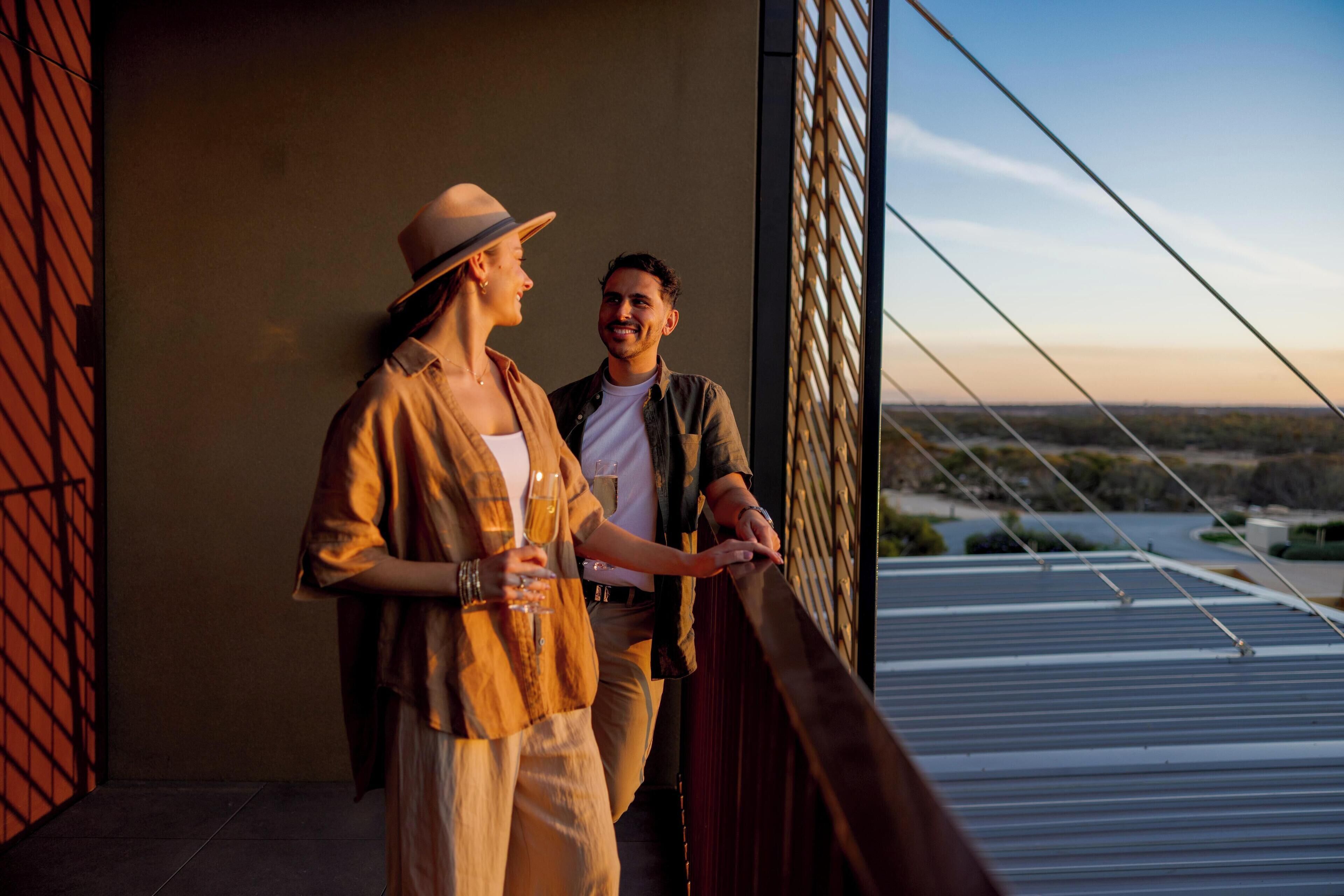 A couple standing on a balcony with a view of a cityscape.