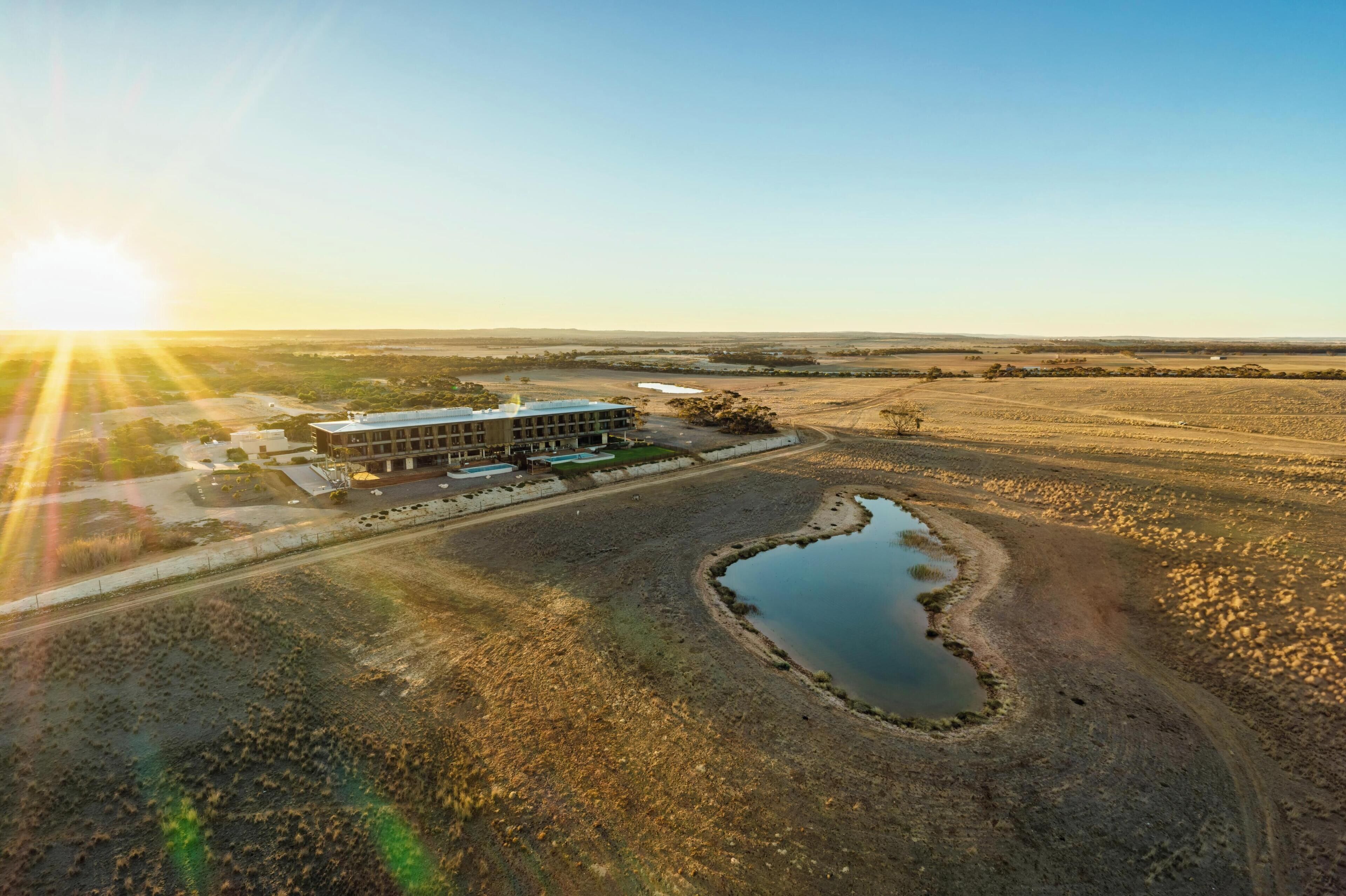 An aerial view of a building with a parking lot and a small pond.