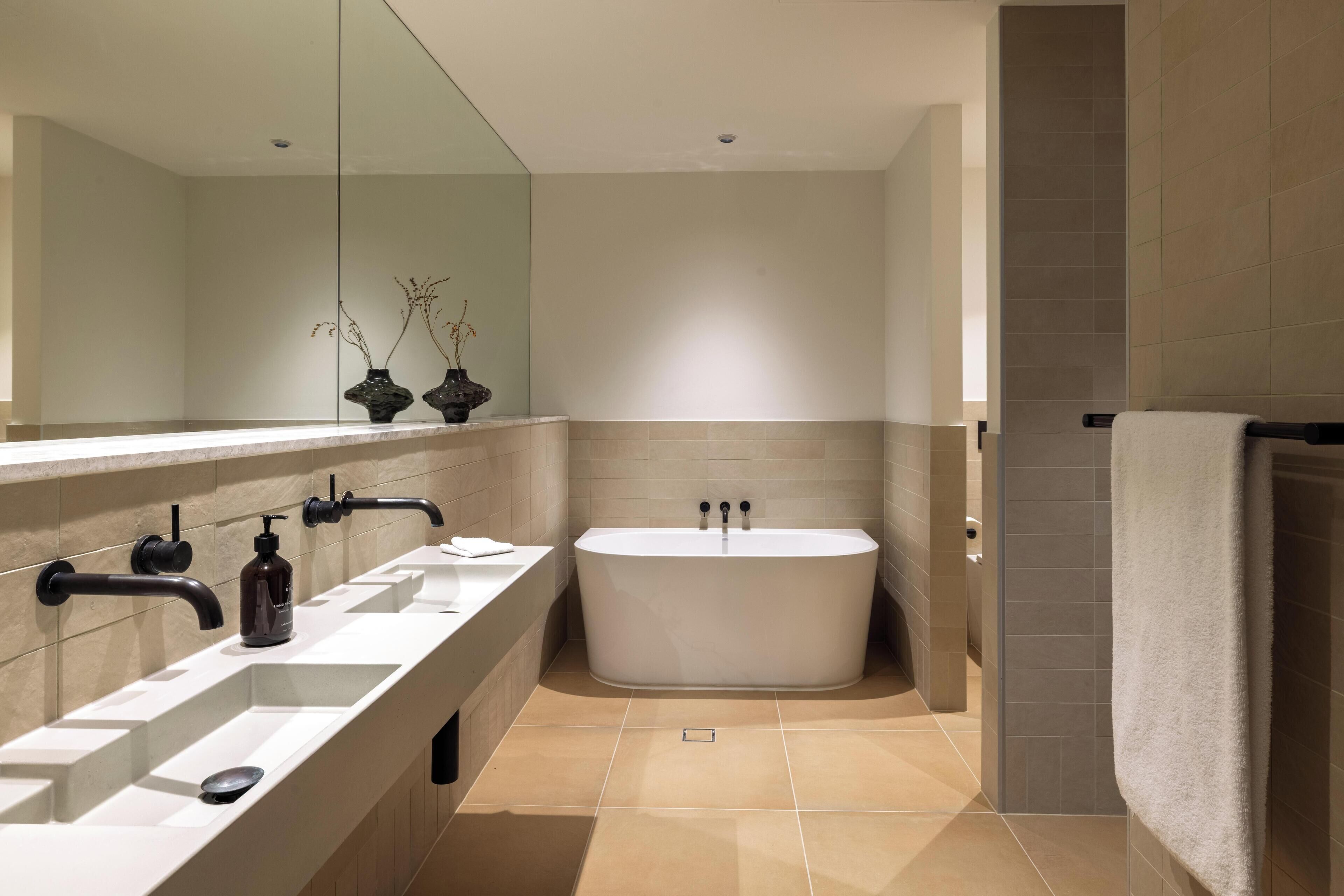 A modern bathroom with a large bathtub, two sinks, and a mirror.