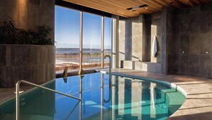 A modern indoor pool with clear glass walls, a wooden ceiling, and a view of the beach. - Monarto Safari Resort (Monarto)