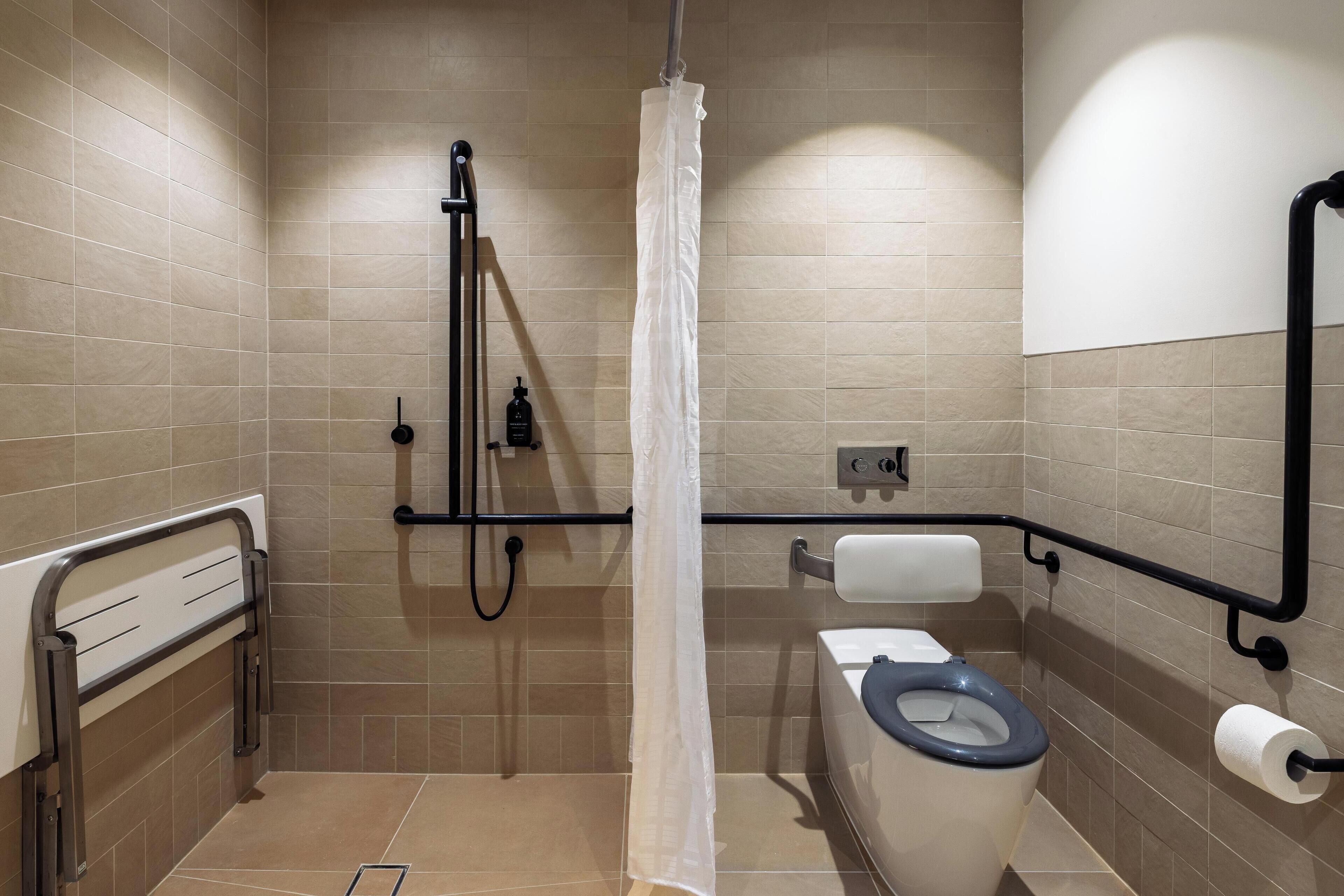 A bathroom with a shower, toilet, and handrail.