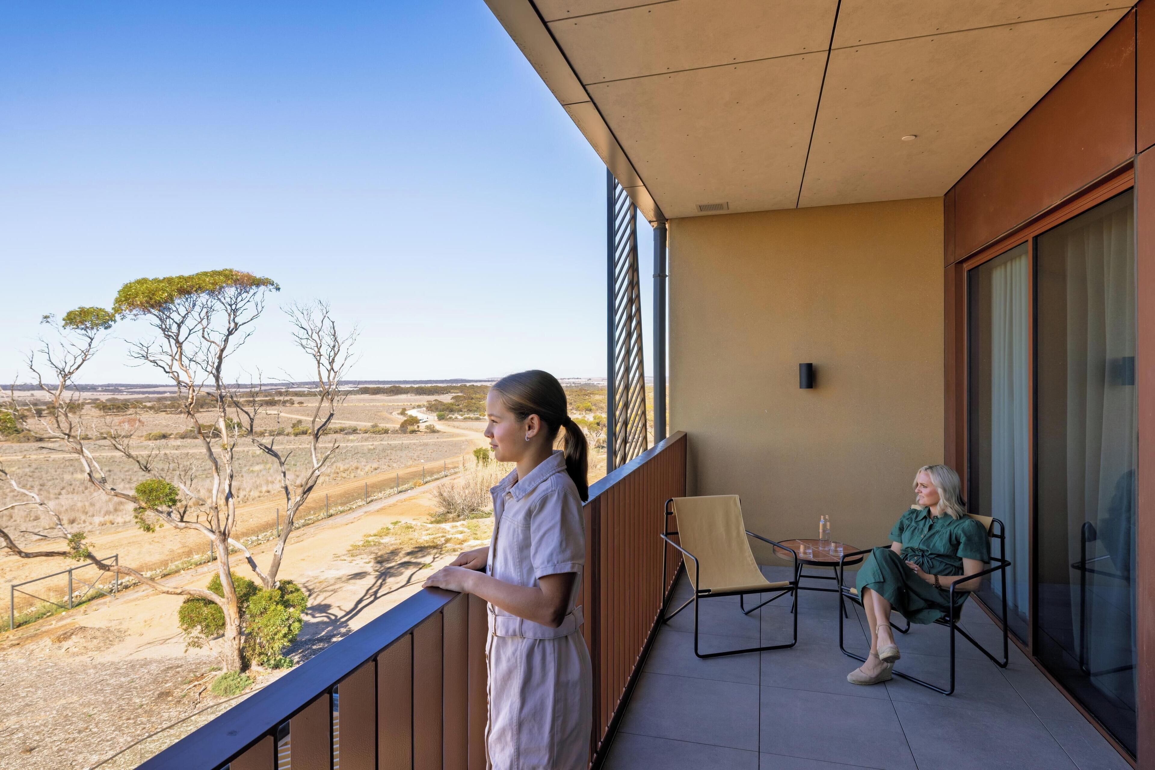 A balcony with a clear view of a dry landscape, a table with a chair, and a person sitting in a chair.