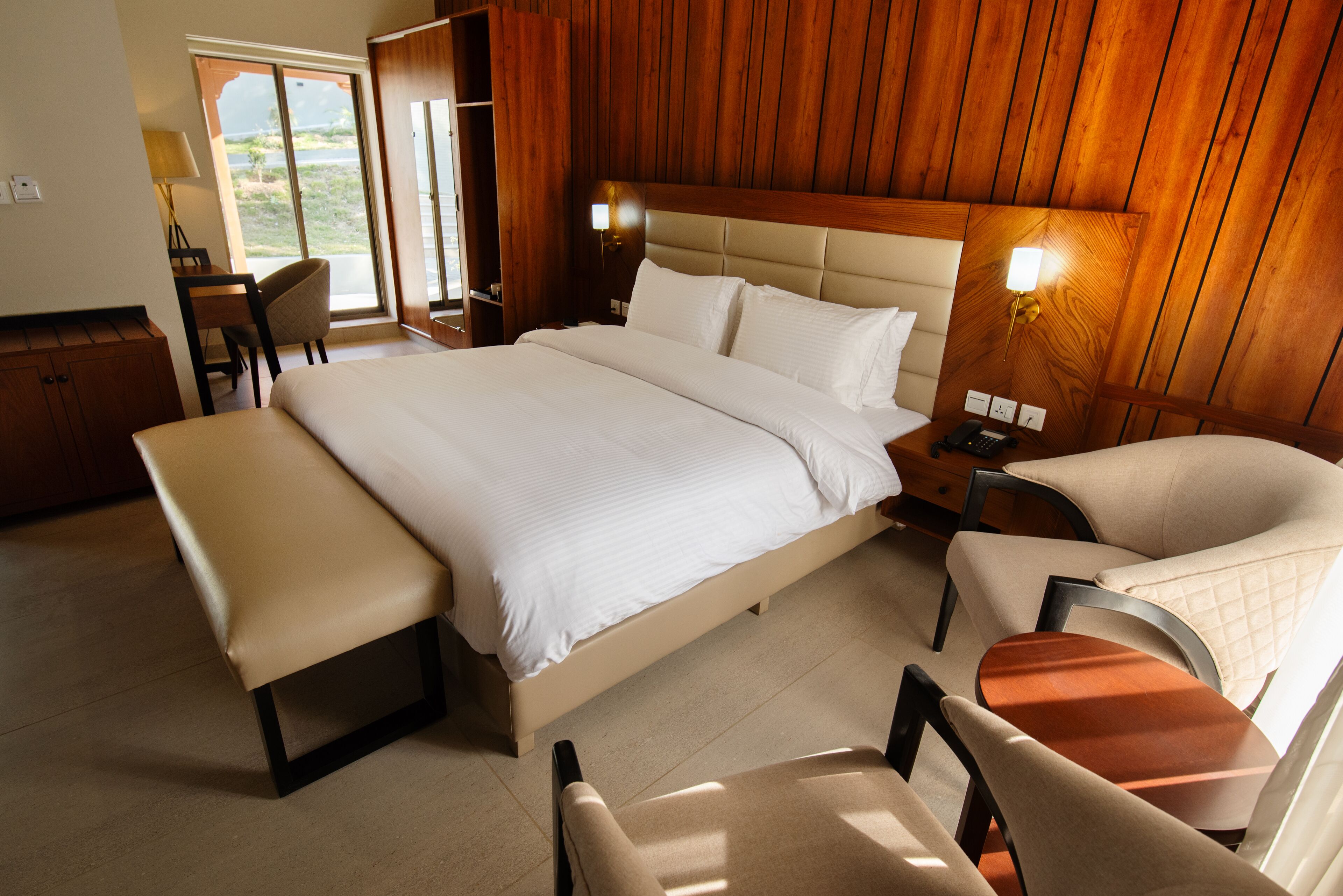A spacious bedroom with a large bed, a bench, two chairs, and a desk.