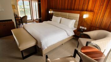 A spacious bedroom with a large bed, a bench, two chairs, and a desk.