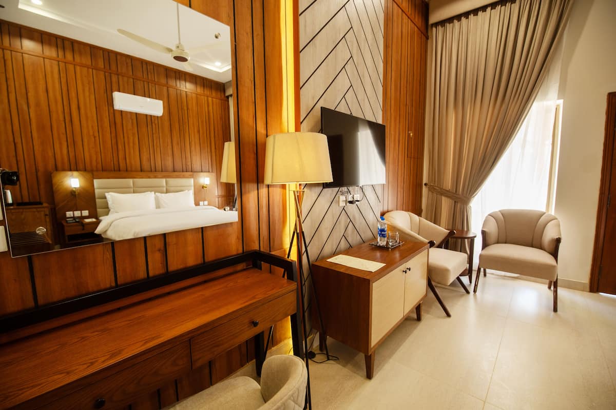 Une chambre d’hôtel avec une tête de lit en bois, un lit, un bureau avec une lampe, une chaise et un téléviseur.