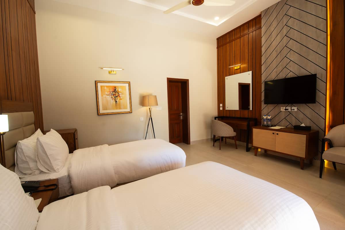 Une chambre d’hôtel avec deux lits, un bureau, une chaise, une télévision et un grand miroir.