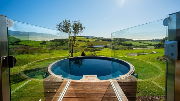 A hot tub with a wooden deck, surrounded by a glass enclosure, overlooking a lush green landscape with hills and a clear sky. - Luxury Coastal Vineyard Escape | The Canopy | Crooked River Estate (Gerringong)