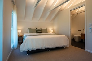 Un dormitorio con una cama grande, lámparas de noche, una ventana con cortinas y una puerta que da a un baño.