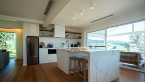 A modern kitchen with a large island, wooden flooring, and a view of the countryside. - Luxury Coastal Vineyard Escape | The Canopy | Crooked River Estate (Gerringong)