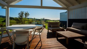 A covered outdoor area with a wooden deck, a round table with chairs, a sofa, and a wooden coffee table. - Luxury Coastal Vineyard Escape | The Canopy | Crooked River Estate (Gerringong)