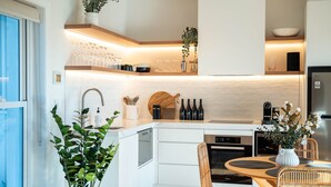 Eine moderne Küche mit weißen Schränken, einem eingebauten Backofen und einem Essbereich mit rundem Tisch und Korbstühlen.