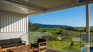 Ein Balkon mit Holzterrasse, einer Couch und einem Sessel, mit Blick auf eine grüne Landschaft aus Feldern und Hügeln.