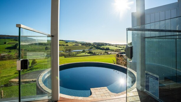 Ein moderner Außenpool mit Glasveranda, der einen malerischen Ausblick auf sanfte Hügel und einen klaren Himmel bietet.