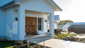 A modern house with a white exterior, a wooden front door, and a covered porch. - Luxury Coastal Vineyard Escape | Flame Vista | Crooked River Estate (Gerringong)