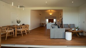 A spacious living area with a wooden dining table, wicker chairs, a grey sofa, and a round coffee table. - Luxury Coastal Vineyard Escape | Flame Vista | Crooked River Estate (Gerringong)