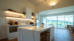 A modern kitchen with a marble island, built-in appliances, and a large window offering a view of the countryside. - Luxury Coastal Vineyard Escape | Flame Vista | Crooked River Estate (Gerringong)