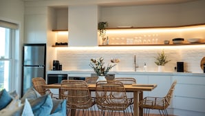 A modern kitchen with a central island, white cabinetry, and a dining area with wicker chairs. - Luxury Coastal Vineyard Escape | Fig View | Crooked River Estate (Gerringong)