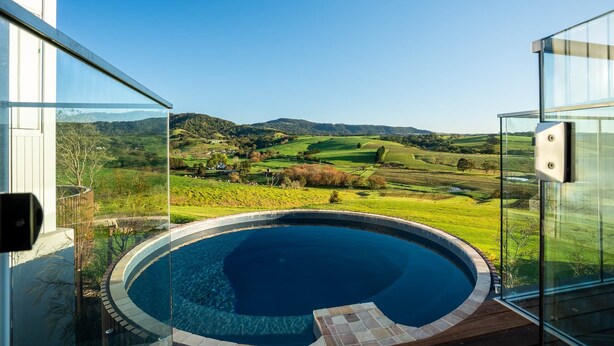 A modern outdoor swimming pool with a clear view of a lush green landscape and distant hills. - Luxury Coastal Vineyard Escape | Fig View | Crooked River Estate (Gerringong)