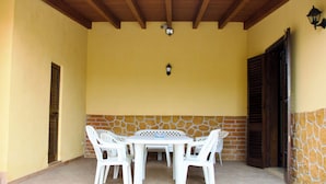 A covered patio with a stone wall, a wooden ceiling, and a table with chairs. - Villa La Perla (Marsala)