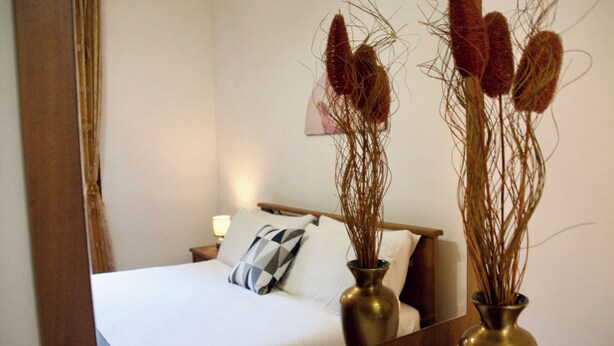 A neatly made bed with a pillow, two vases with dried plants, and a mirror reflecting the room. - Villa La Perla (Marsala)