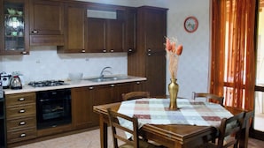 A kitchen with wooden cabinets, a stove, sink, and a dining table with chairs. - Villa La Perla (Marsala)