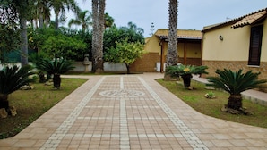 A paved pathway leading to a building with a tiled roof and stone walls, surrounded by palm trees and greenery. - Villa La Perla (Marsala)