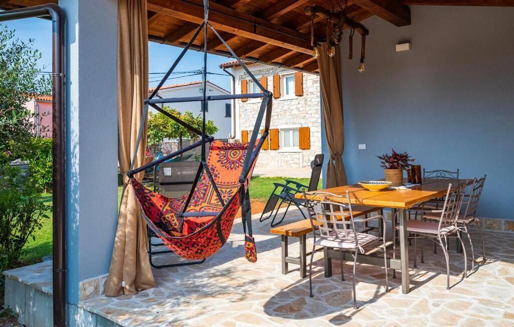 Een terras met een hangstoel, een tafel met stoelen en uitzicht op een stenen gebouw.