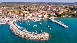 An aerial view of a coastal town with a marina, stone pier, and buildings with red roofs.