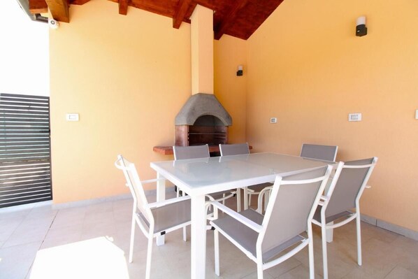 A patio with a table and chairs, a stone oven, and a wooden ceiling.