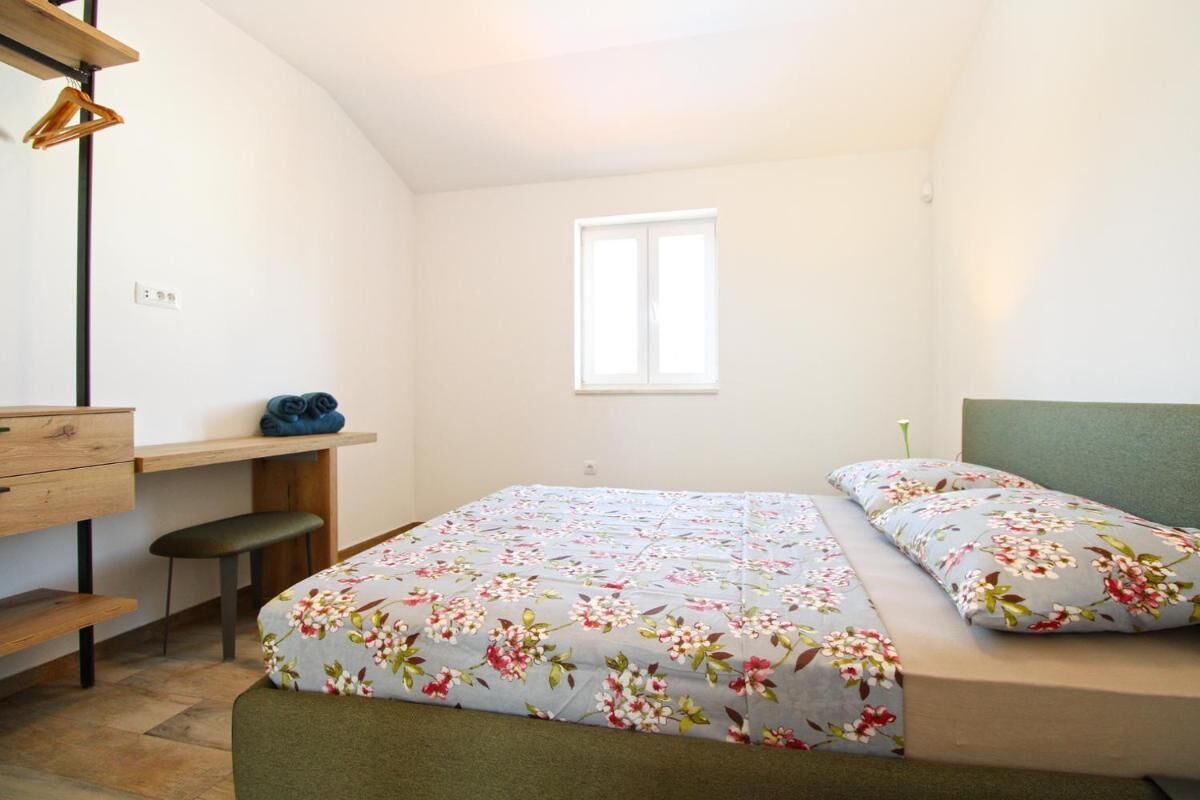 A bedroom with a bed, a desk, and a chair. There is a window providing natural light.