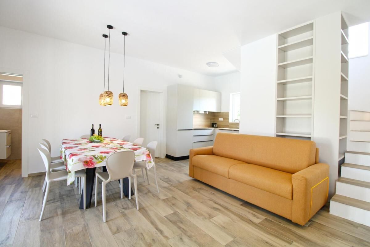 A modern living room with a sofa, dining table, chairs, and pendant lights.