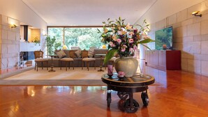 A spacious living room with a wooden floor, a large window, a sofa set, a coffee table with a vase of flowers, and a flat-screen TV mounted on the wall. - Caesar Gora Club Hakone (Hakone)