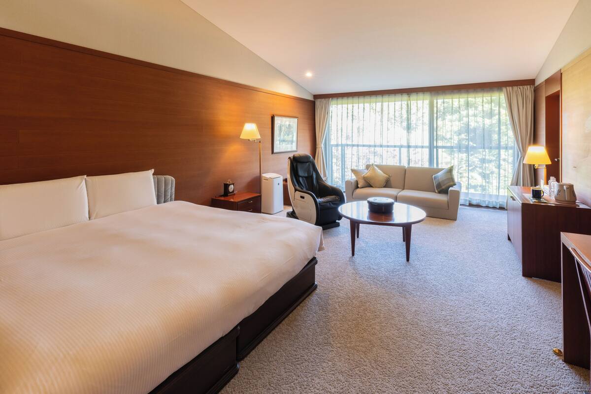 Quarto de hotel com uma cama grande, um sofá, uma cadeira, uma mesa pequena e uma escrivaninha.