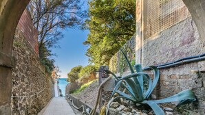 Een smal stenen pad langs gebouwen, dat uitkomt op uitzicht over de zee.