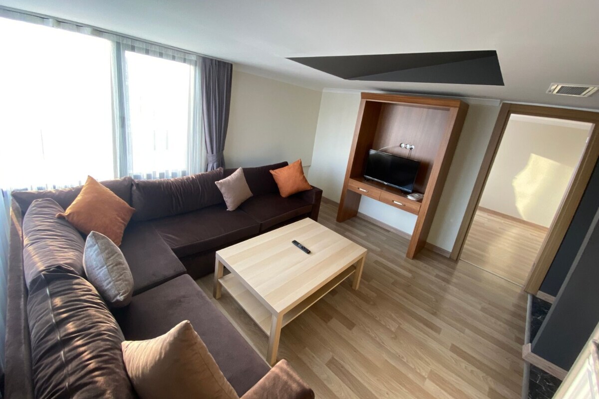 Una sala moderna con un sofá modular, un mueble de televisión de madera y una mesa de centro de madera clara.