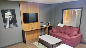 A compact living space with a wooden desk, a flat-screen TV, a red sofa, and a small white table. - 216 F&B Suites (Istanbul)