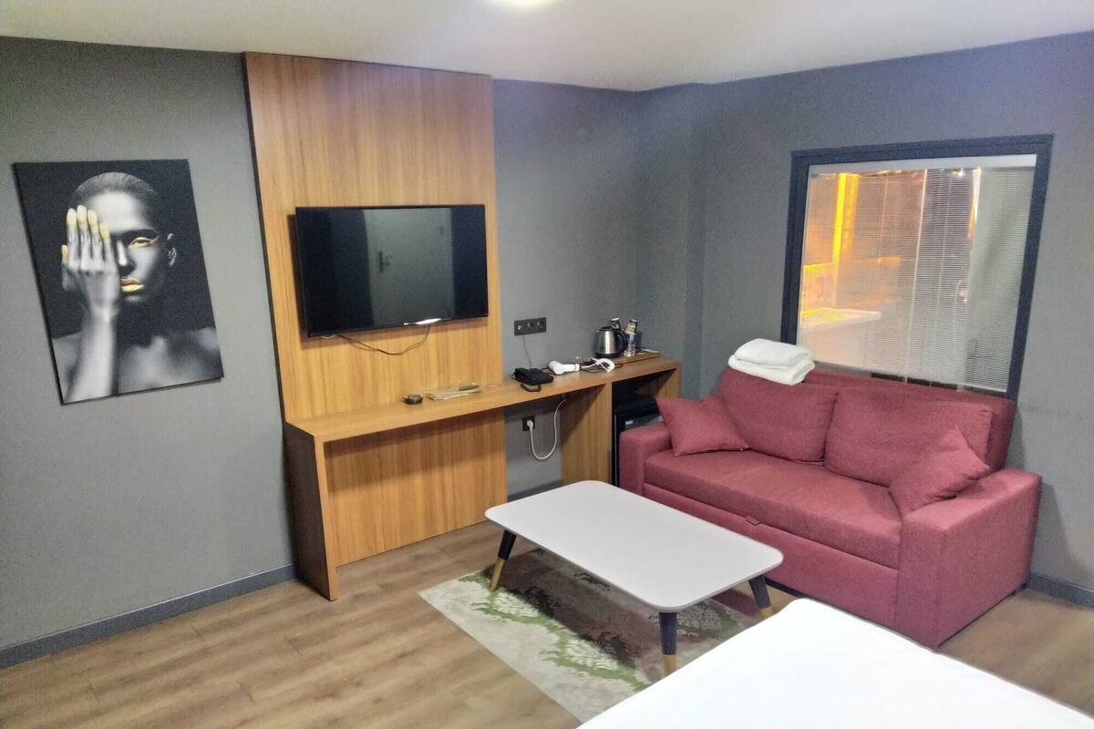 A compact living space with a wooden desk, a flat-screen TV, a red sofa, and a small white table.