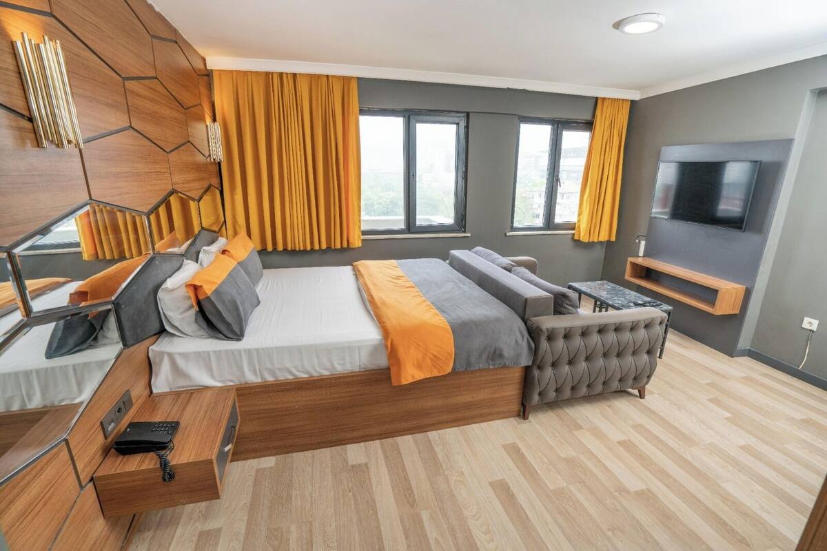 A modern bedroom with a large bed, a sofa, a TV, and a desk.