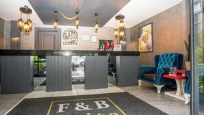 A hotel reception area with a reception desk, a '216 Suites' sign, a 'Tip Box' sign, and a blue chair. - 216 F&B Suites (Istanbul)