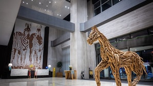 A spacious lobby with a large giraffe sculpture, a high ceiling with hanging lights, and a large wall mural. - Shanshui S Hotel  (Wuhan)