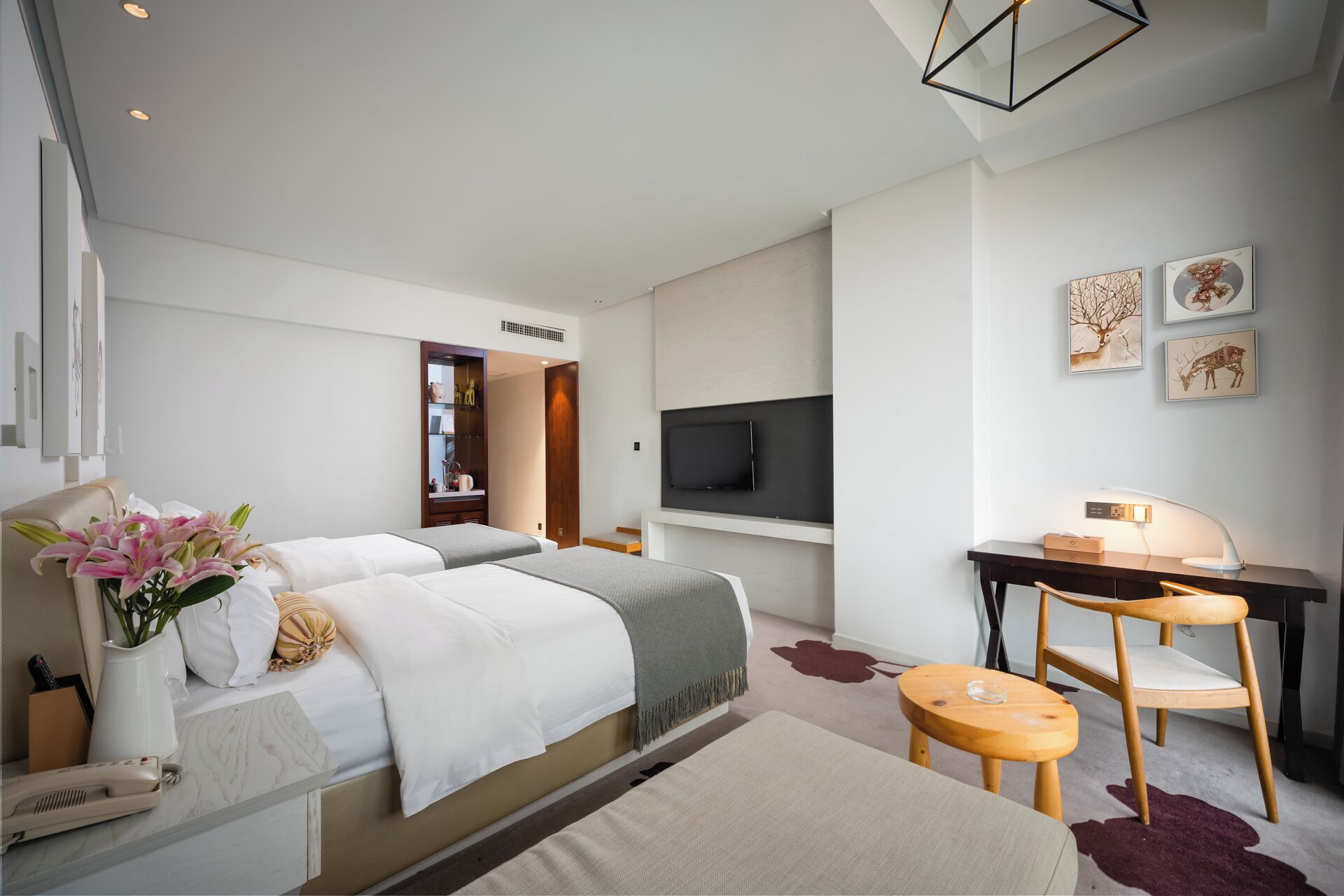 A hotel room with two beds, a desk, a TV, and artwork on the wall.