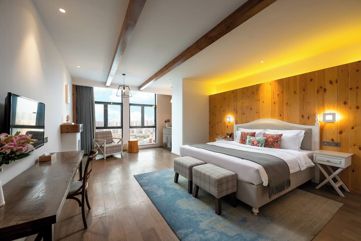 A modern hotel room with a large bed, a dining area, and a view of the city.