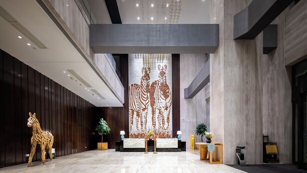 A spacious lobby with a reception desk, a large abstract wall art, and a wooden sculpture of a giraffe. - Shanshui S Hotel  (Wuhan)