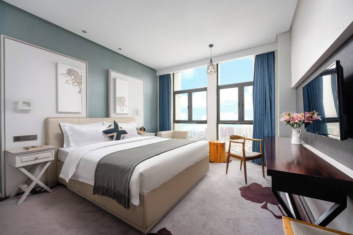 A modern hotel room with a large bed, a desk, and a TV.