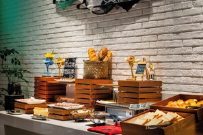 A buffet with various food items, including bread, pastries, and sushi, displayed on wooden crates and tables against a white brick wall. - Shanshui S Hotel  (Wuhan)