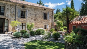 A stone building with a tiled roof, a reception area, and a garden with various plants and a bench.