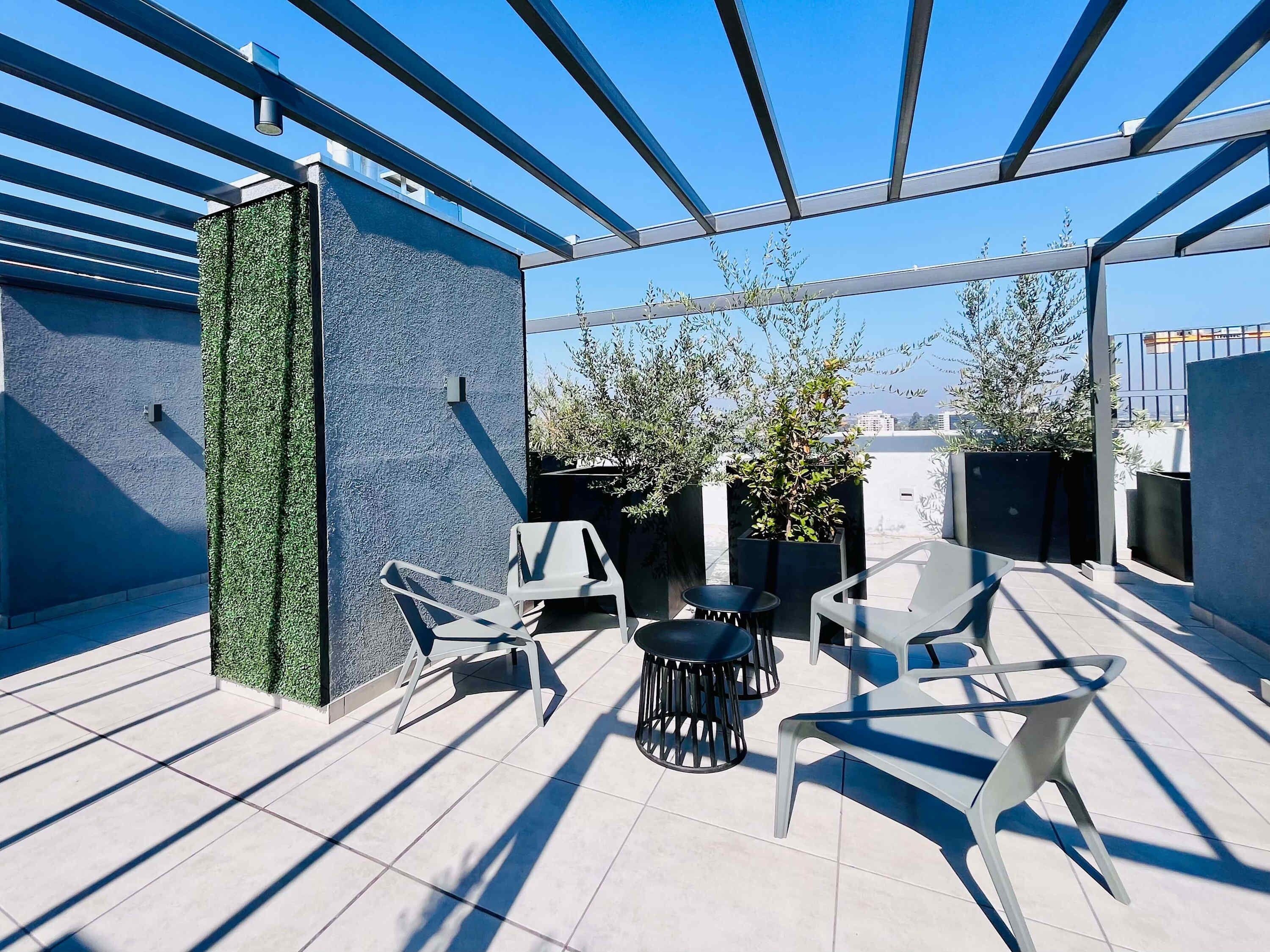 En takterrass med modern design, med en sittgrupp bestående av stolar och bord, omgiven av planterade växter och med en fri utsikt över stadens silhuett.