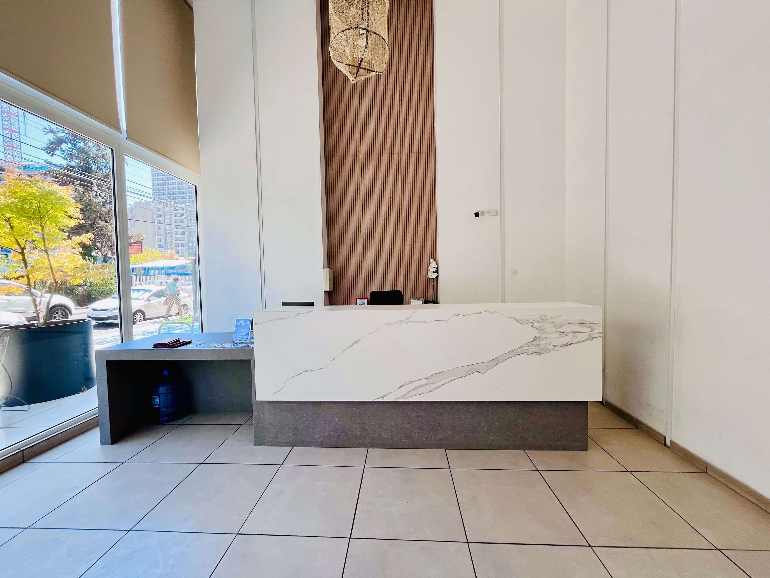 A modern hotel room with a marble reception desk, large windows with a view of the street, and a potted plant.