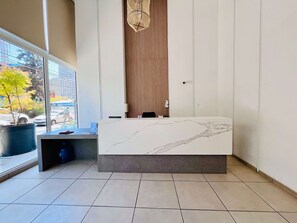 A modern hotel room with a marble reception desk, large windows with a view of the street, and a potted plant. - 1BR La Florida - Free Parking, Pool & Metro (La Florida)
